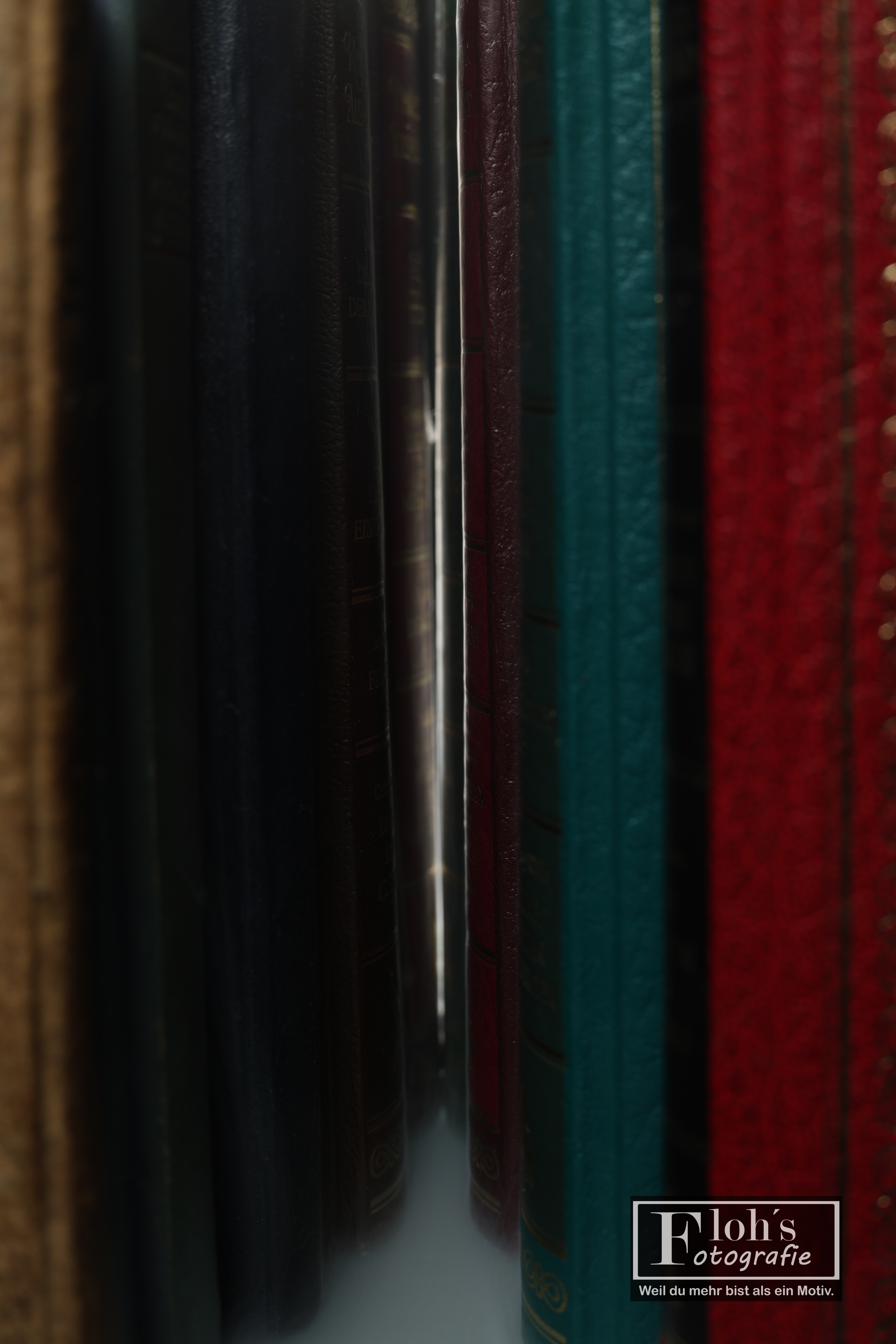 Schmaler Lichtspalt zwischen dicht nebeneinanderstehenden Büchern mit dunklen, türkisfarbenen und roten Einbänden.