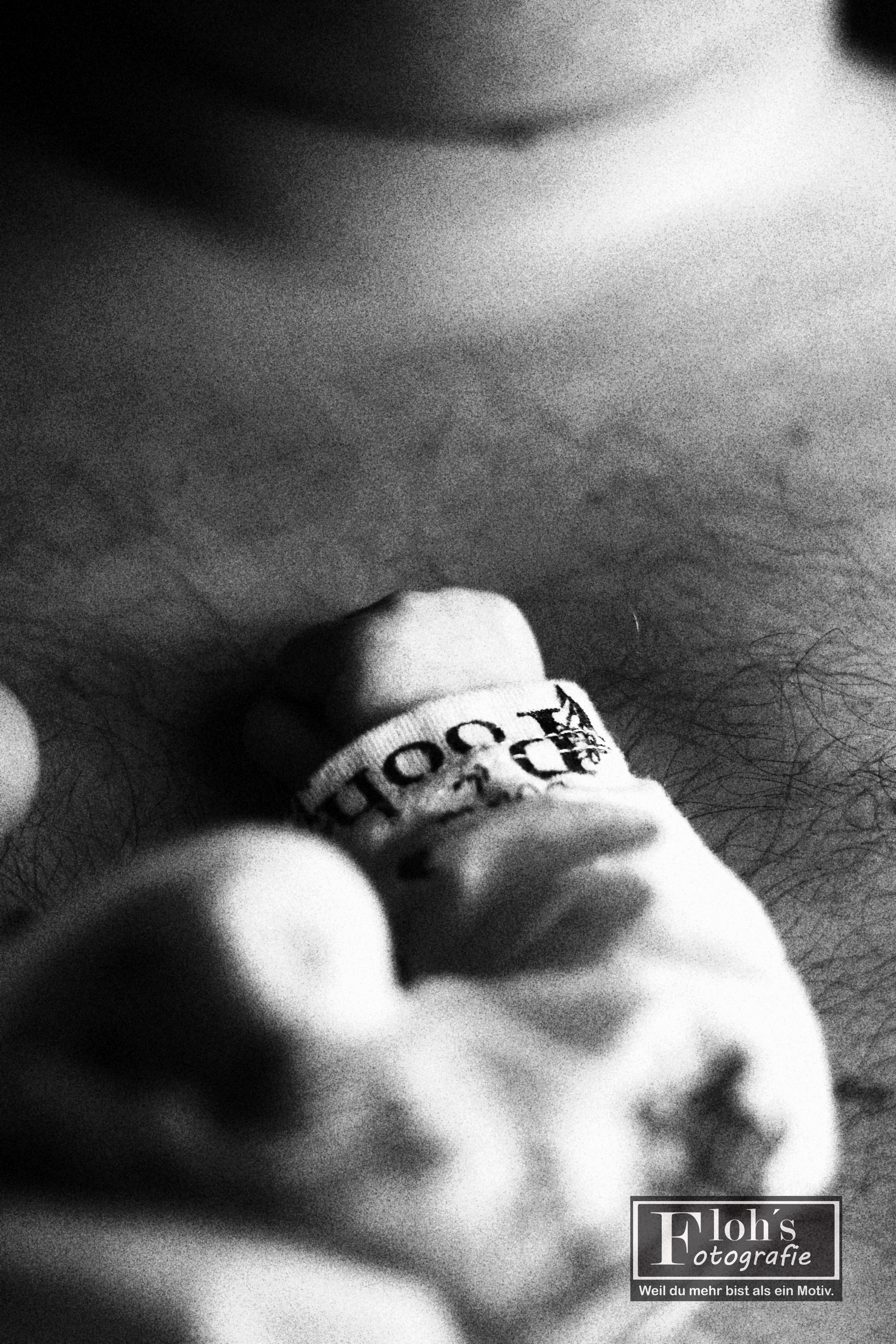 Körnige Schwarz-Weiß-Nahaufnahme eines Babys an der Brust eines Erwachsenen, mit einer Hand im unscharfen Vordergrund.