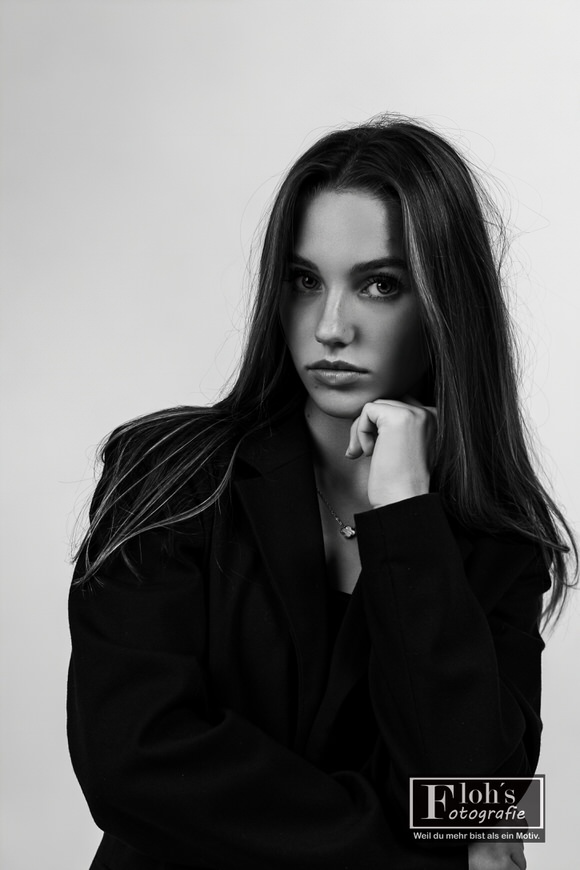 Schwarz-Weiß-Porträt von Christina im schwarzen Blazer, mit einer Hand unter dem Kinn und Blick in die Kamera.