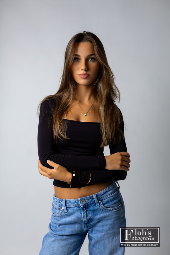 Christina in schwarzem Langarmtop und blauer Jeans, mit verschränkten Armen und direktem Blick in die Kamera.