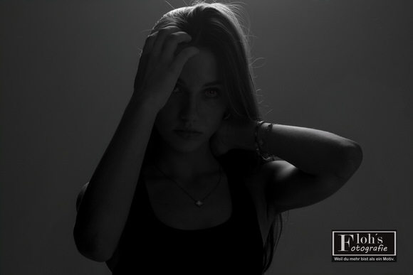 Dunkles Schwarz-Weiß-Porträt von Christina mit einer Hand im Haar und einer im Nacken. Gegenlicht hebt ihre Konturen hervor.