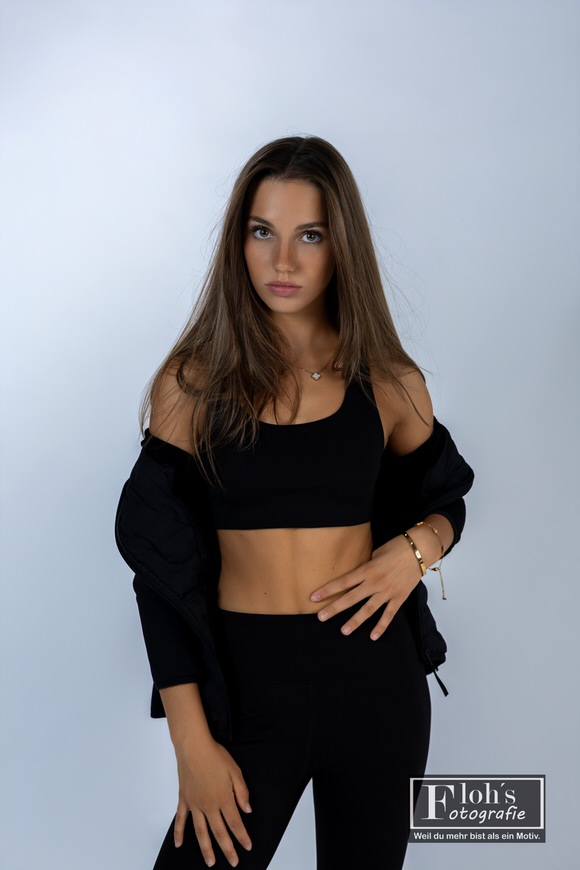 Christina im schwarzen Sportoutfit mit locker über den Armen liegender Jacke und direktem Blick in die Kamera.