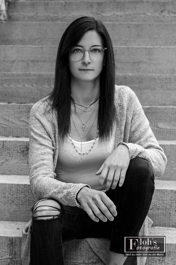 Schwarz-Weiß-Portrait von Lisa auf einer Treppe, mit einem aufgestellten Knie und direktem Blick in die Kamera.