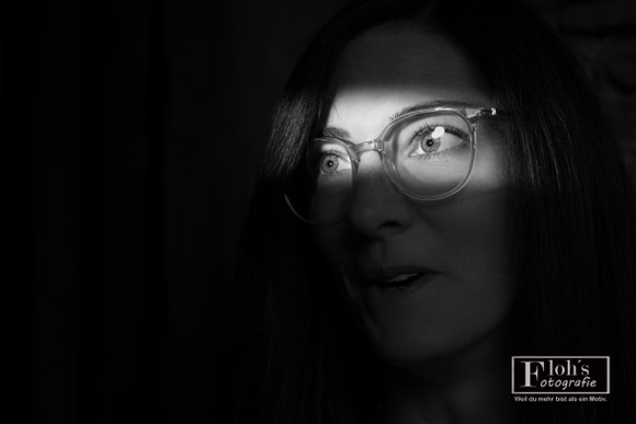 Schwarz-Weiß-Portrait von Lisa mit Brille, deren Augenpartie von einem Lichtstreifen beleuchtet wird, während ihr Gesicht überwiegend im Schatten liegt.