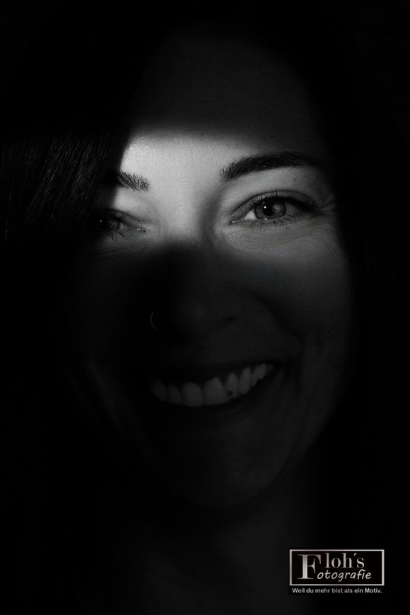 Schwarz-Weiß-Nahaufnahme von Lisa mit breitem Lächeln und einem hellen Lichtstreifen über ihrer Augenpartie.
