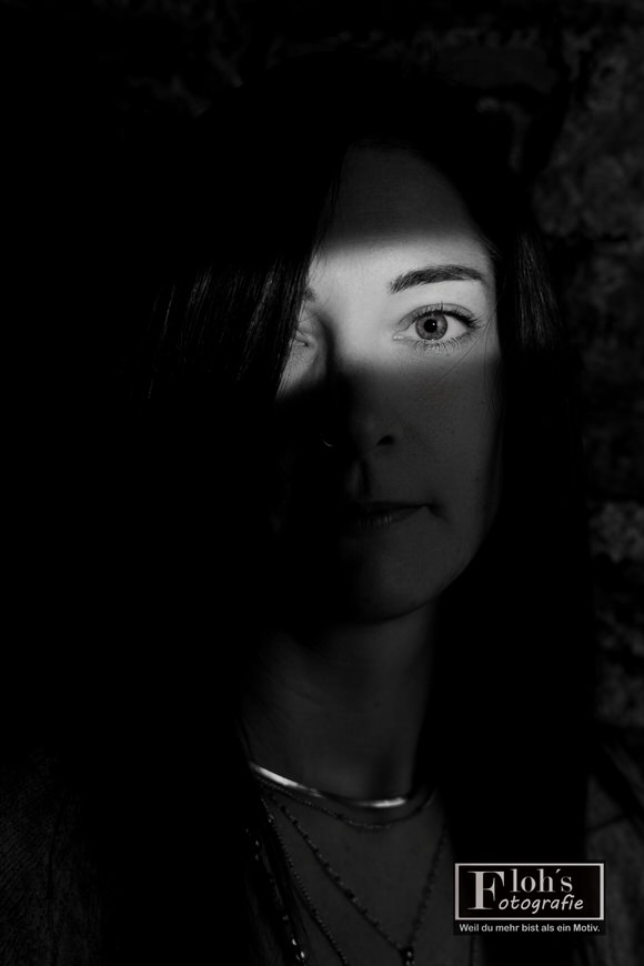 Schwarz-Weiß-Portrait von Lisa mit direktem Blick und einem Lichtstreifen über den Augen, wobei Haare einen Teil ihres Gesichts verdecken.