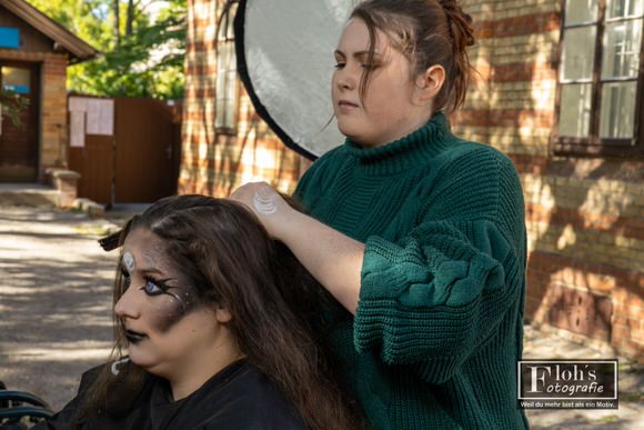 Jessi richtet Vicis Haare nach dem Schminken. Hinter den beiden steht ein runder Reflektor am Set.