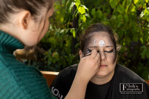 Jessi arbeitet an Vicis Hexen-Make-up mit dunklen Schattierungen, geschwungenen Augenlinien und hellen Mondsymbolen auf der Stirn.
